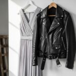 Čierna kožená ramoneska na drevenom vešiaku vedľa pastelovej šaty na bielom pozadí